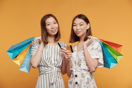 Two happy young Asian female twin consumers with paperbags and credit cardsの写真素材