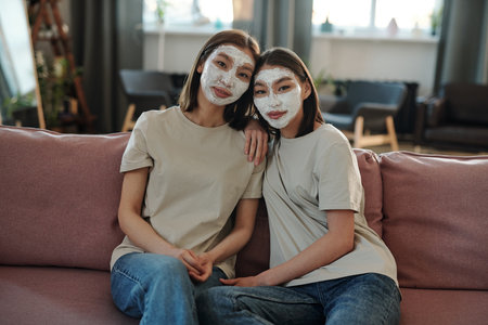 Two young affectionate brunette females having facial clay mask at homeの写真素材