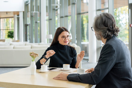 Contemporary elegant businesswoman in eyeglasses sharing ideas with colleagueの写真素材