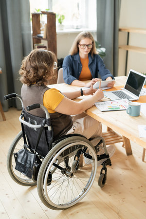 Young disable female accountant in wheelchair pointing at financial document