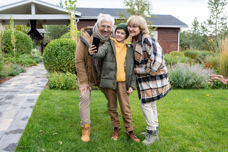 Happy youngster in casualwear and his affectionate grandparents making selfie