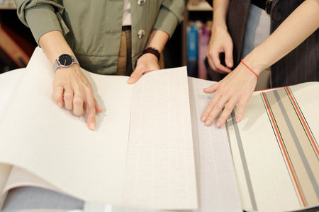 Hands of young female shop assistant helping client to choose new wallpapersの写真素材