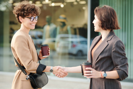 Two young cheerful females or business partners greeting each other by handshakeの写真素材
