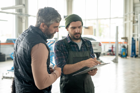 Serious bearded male client of contemporary car service looking at documentの写真素材