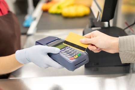 Cashier holding payment terminal while one of consumers paying by credit cardの写真素材