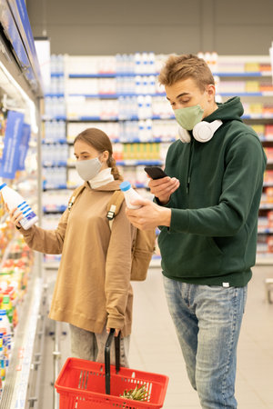 Two teenage siblings in casualwear and protective masks choosing dairy productsの写真素材