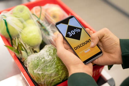 Hands of young man holding smartphone with discount coupon on the screenの写真素材