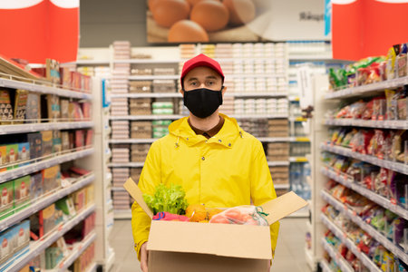 Young male courier in uniform and protective mask standing between displaysの写真素材