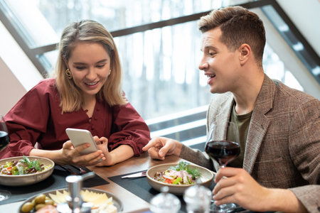 Elegant blond girl with smartphone discussing curious video with her boyfriend
