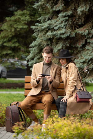 Happy young man in stylish warmwear and his girlfriend watching online video