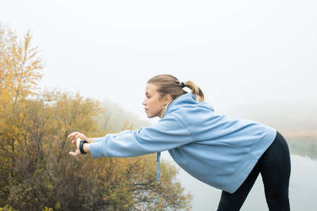 Young sportswoman in hoodie and leggins stretching her arms in front of herself