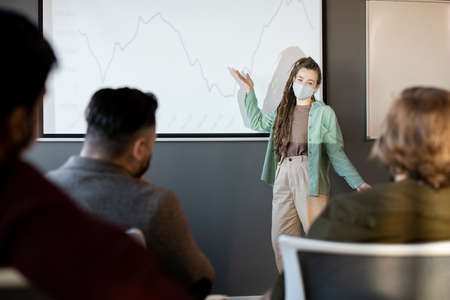Confident business coach in casualwear and protective mask making presentation