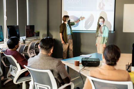 One of two designers in protective masks pointing at new model of smartwatch