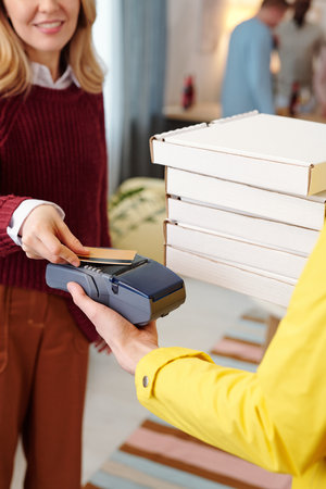 Young smiling blond female holding credit card over screen of payment machine
