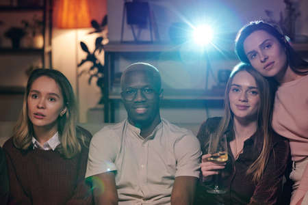 Group of young intercultural friends relaxing in living-room in front of camera