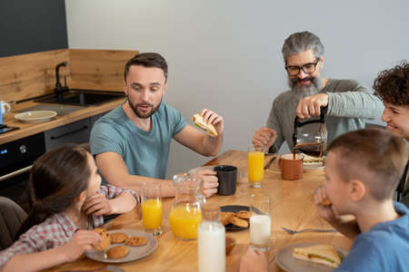 Happy family of five sitting by table in the kitchen and enjoying breakfastの写真素材