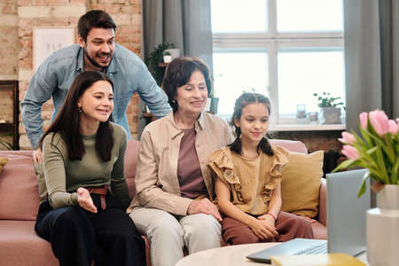 Happy family of four communicating with their friends through video chat at homeの写真素材