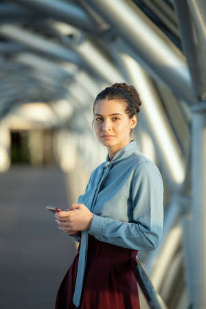 Young elegant brunette female delegate looking at you while using smartphone