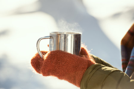 Hands of young female in warm winterwear holding metallic mug with hot teaの写真素材