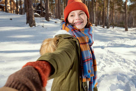Happy young woman in warm winterwear inviting her husband to follow her