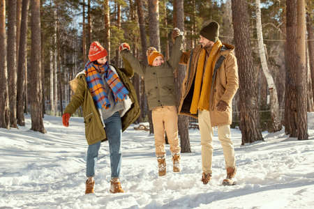Happy young parents in warm winterwear holding jumping little daughter by handsの写真素材