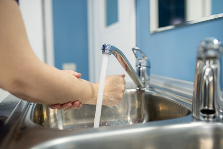 Young female assistant, nurse or surgeon washing hands over one of two sinksの写真素材