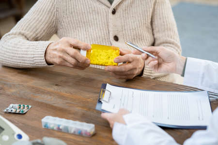 Hands of senior man holding bottle of pills while sitting in front of his doctorの写真素材