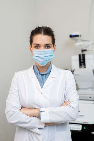 Young successful female ophthalmologist in protective mask and whitecoatの写真素材