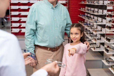 Girl pointing at one of two pairs of eyeglasses held by young female opticianの写真素材