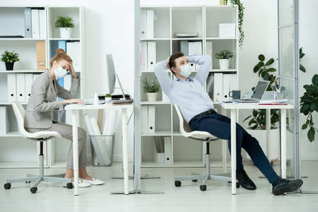 Young businessman in protective mask brainstorming in front of laptop by desk