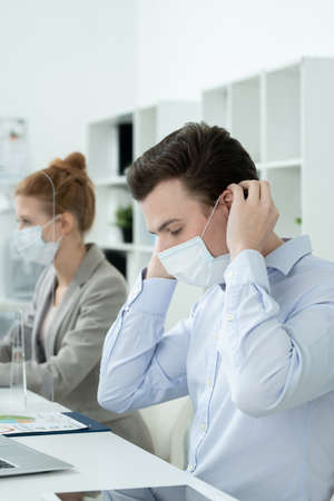 Young businessman putting protective mask by workplace against his colleagueの写真素材
