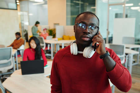 Young serious businessman or designer of African ethnicity talking by smartphone
