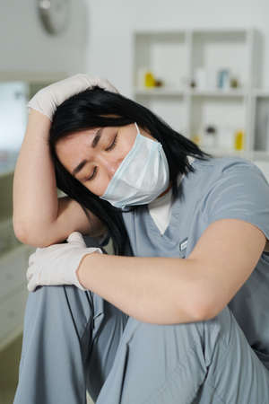 Young tired female clinician sitting in front of camera and touching her head at break after workの写真素材