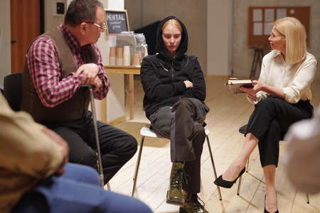 Confident female counsellor and mature male patient looking at troubled girl sitting between them