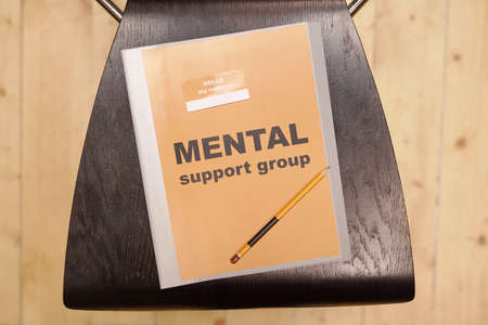 Overview of folder with notice saying mental support group and pencil lying on black wooden chair