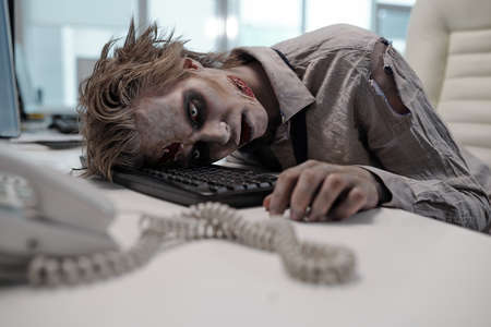 Dead businessman with zombie body painting keeping head on computer keyboard after workingの写真素材