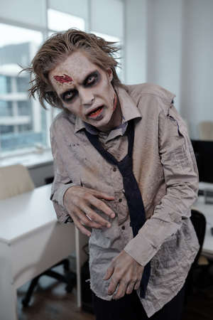 Sulky businessman with zombie body painting looking at you with gloomy facial expression