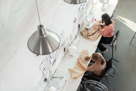 Young seamstress and her disable female colleague working inside large contemporary workshopの写真素材