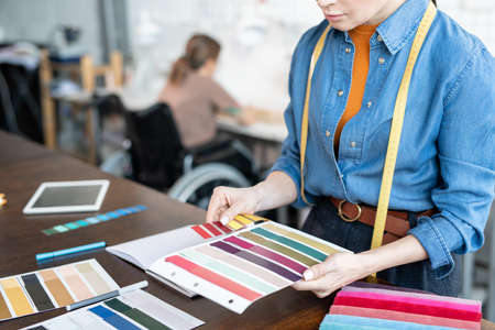 Young fashion designer choosing colors and textile for new collection against disable seamstressの写真素材
