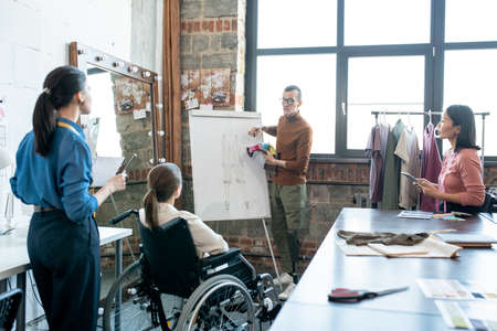 Young disable male designer with textile samples standing by whiteboard while explaining his viewの写真素材