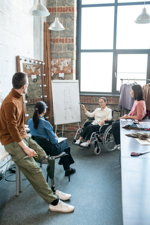Young female creative designer in wheelchair pointing at sketch on whiteboard at seminarの写真素材
