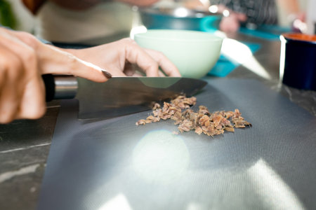 Hand of young woman chopping mushrooms for vegetable stew on plastic board with sharp knife while cooking food by kitchen tableの写真素材