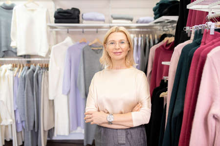 Portrait of mature beautiful saleswoman smiling at camera while standing in the clothing store and waiting for customersの写真素材