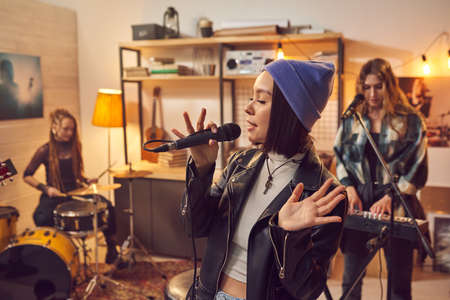 Young woman in stylish clothing singing in microphone with her musical group in the backgroundの写真素材