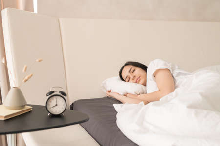 Young gorgeous woman sleeping peacefully in large comfortable double bed in front of small table...
