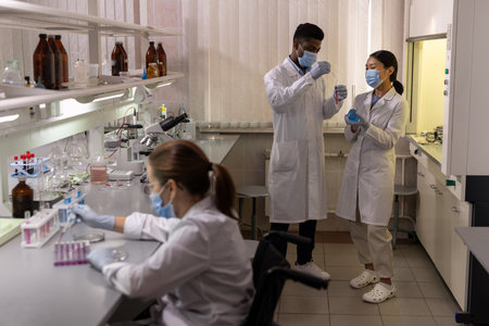 Group of chemists in white coats and masks examining samples and test tubes during teamwork in the...