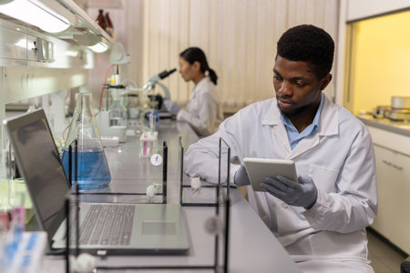 African young scientist using digital tablet and examining two types of mice in the boxes in the...