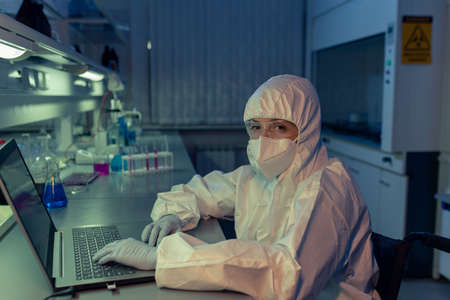 Portrait of mature woman in protective workwear looking at camera while typing on laptop at the...