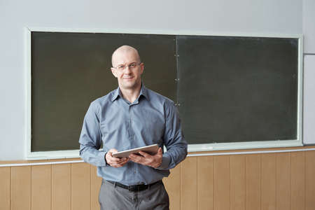 Contemporary professor of university in smart casualwear holding digital tablet while preparing for...