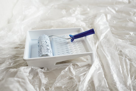White square plastic container with paint and roller on the floor of living-room or other room of new house or flat during home renovationの写真素材